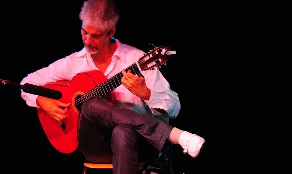 Guitarrista flamenco tocando sentado en un escenario oscuro